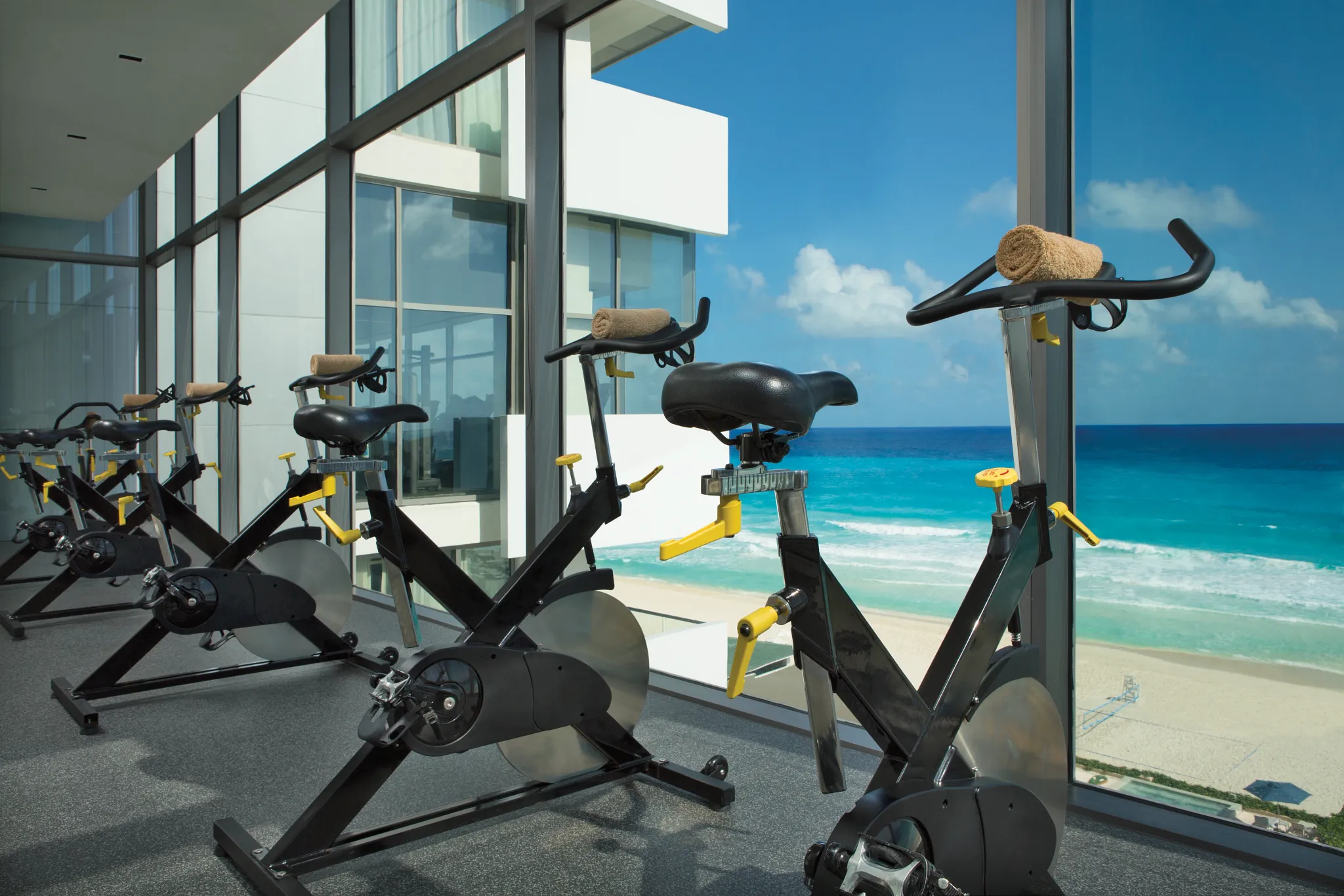 Stationary bikes lined up with panoramic ocean views in the fitness center at Secrets The Vine Cancun.